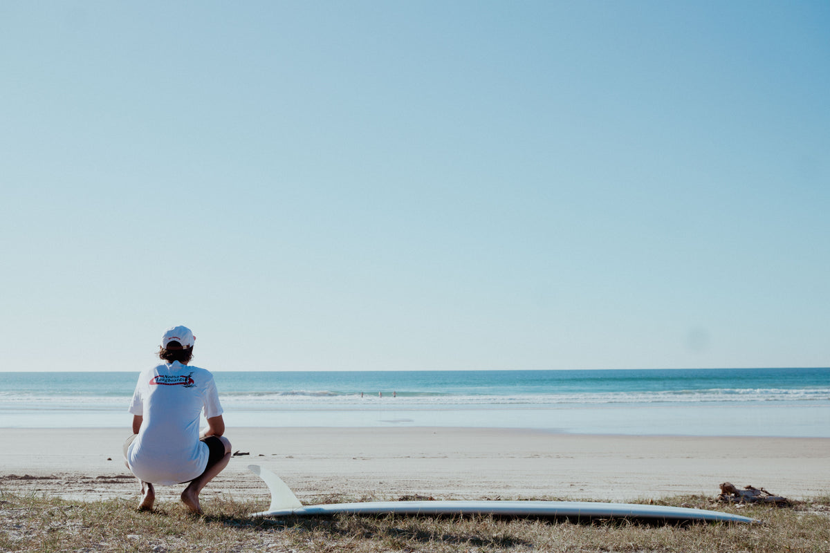 A surfer and longboard overlooking the beach in Noosa