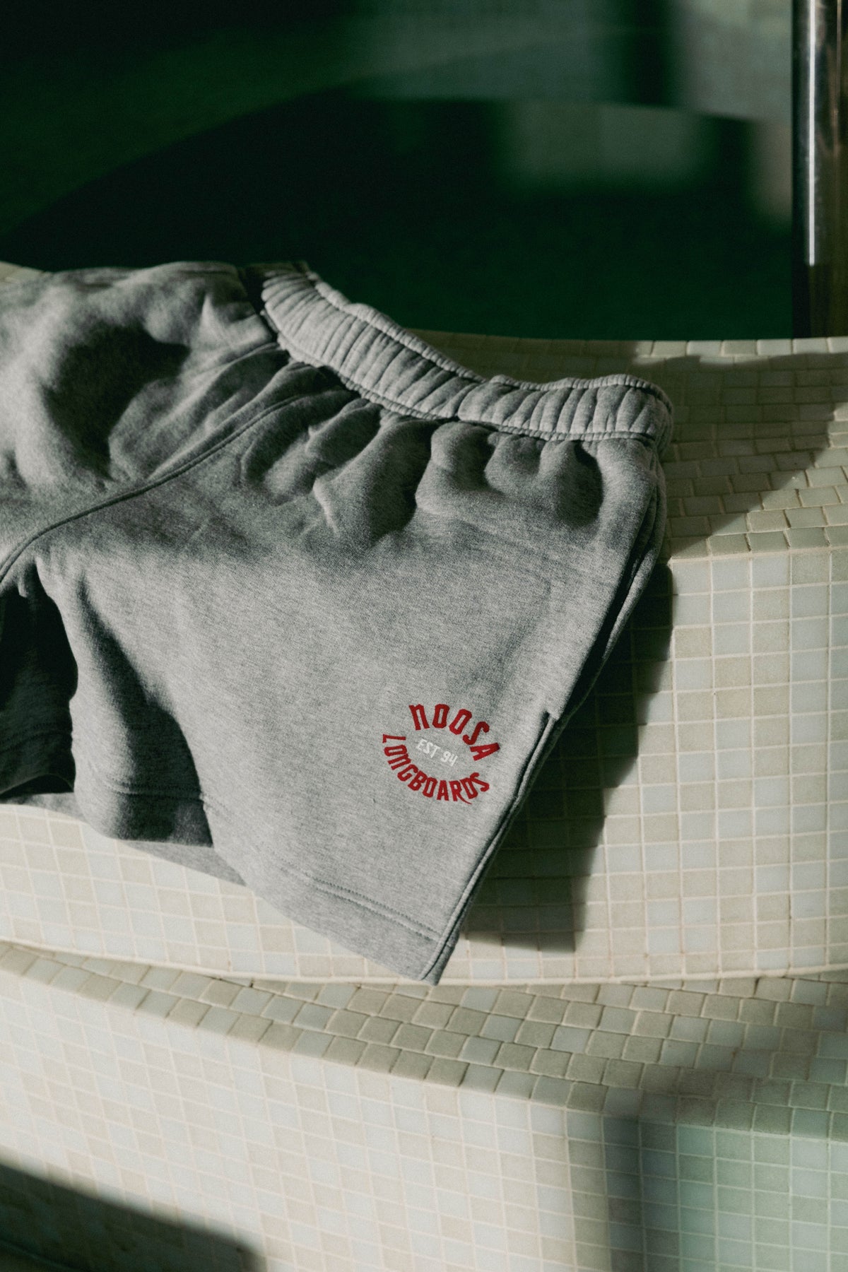 NL Established Track Shorts Grey Marle folded on the curved tiled bench at Domic