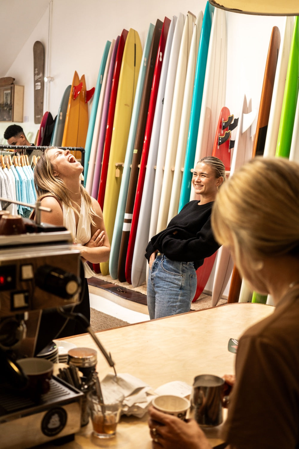 People laughing beside the coffee counter and surfboard racks upstairs